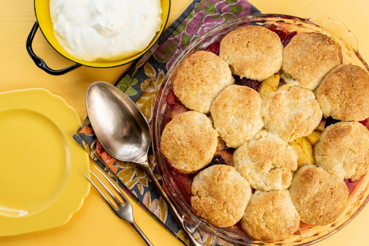 Glass dish of Sour Cream Biscuit Peach and Berry Cobbler.