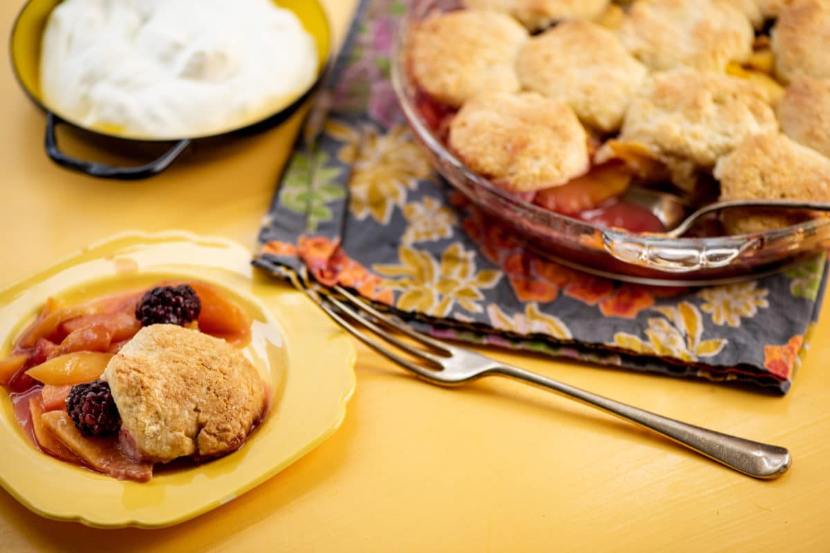 Fork next to a yellow plate of Sour Cream Biscuit Peach and Berry Cobbler.