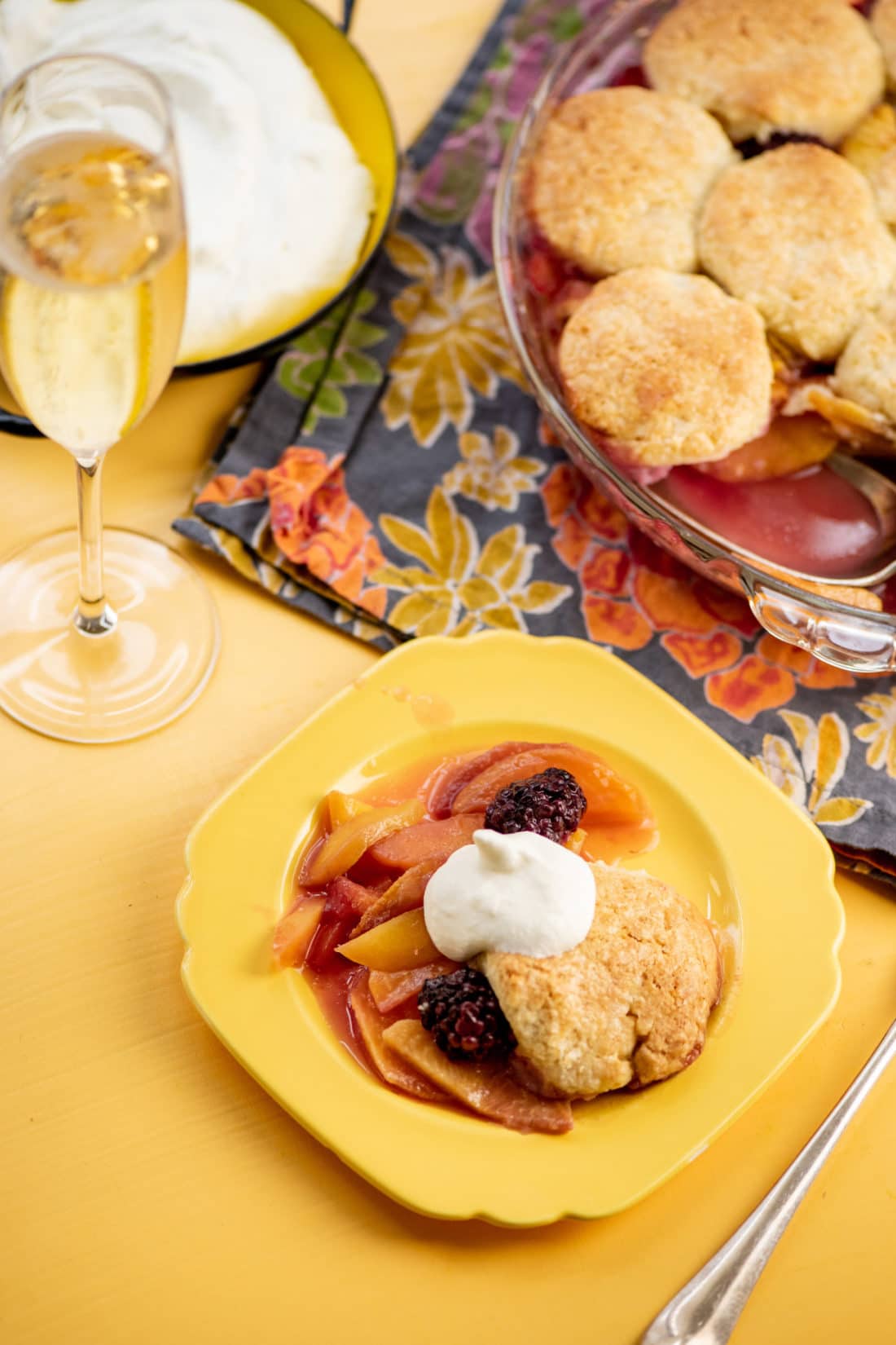 Small yellow plate of Sour Cream Biscuit Peach and Berry Cobbler.