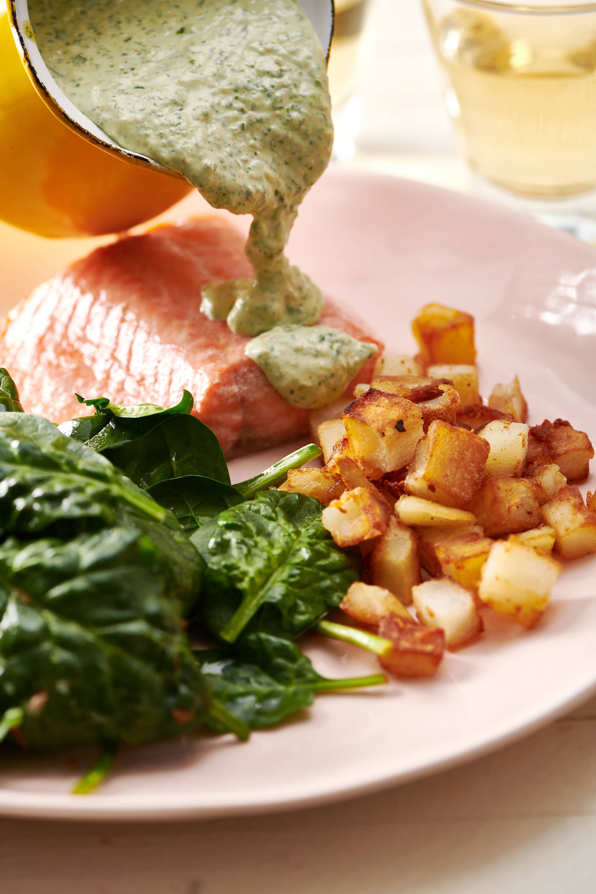Pouring cilantro sauce over poached salmon with sides.