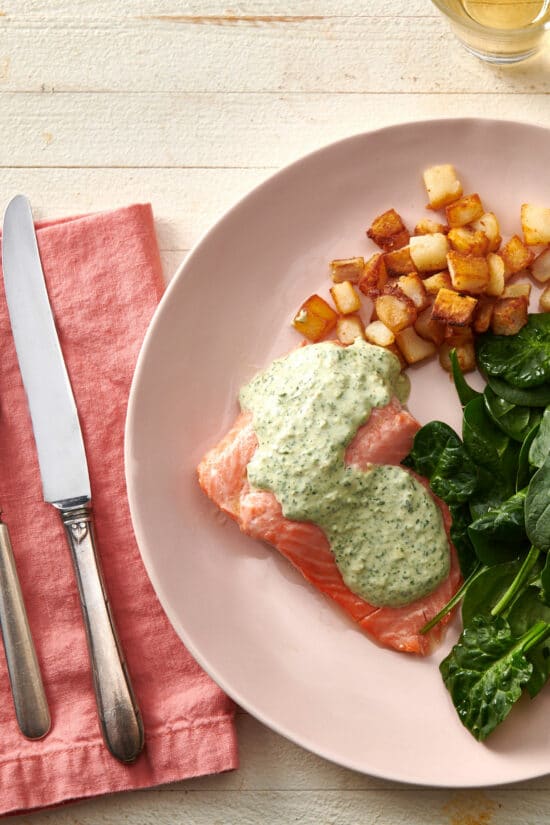 Poached Salmon with Cilantro Sauce on a plate with spinach and potatoes.