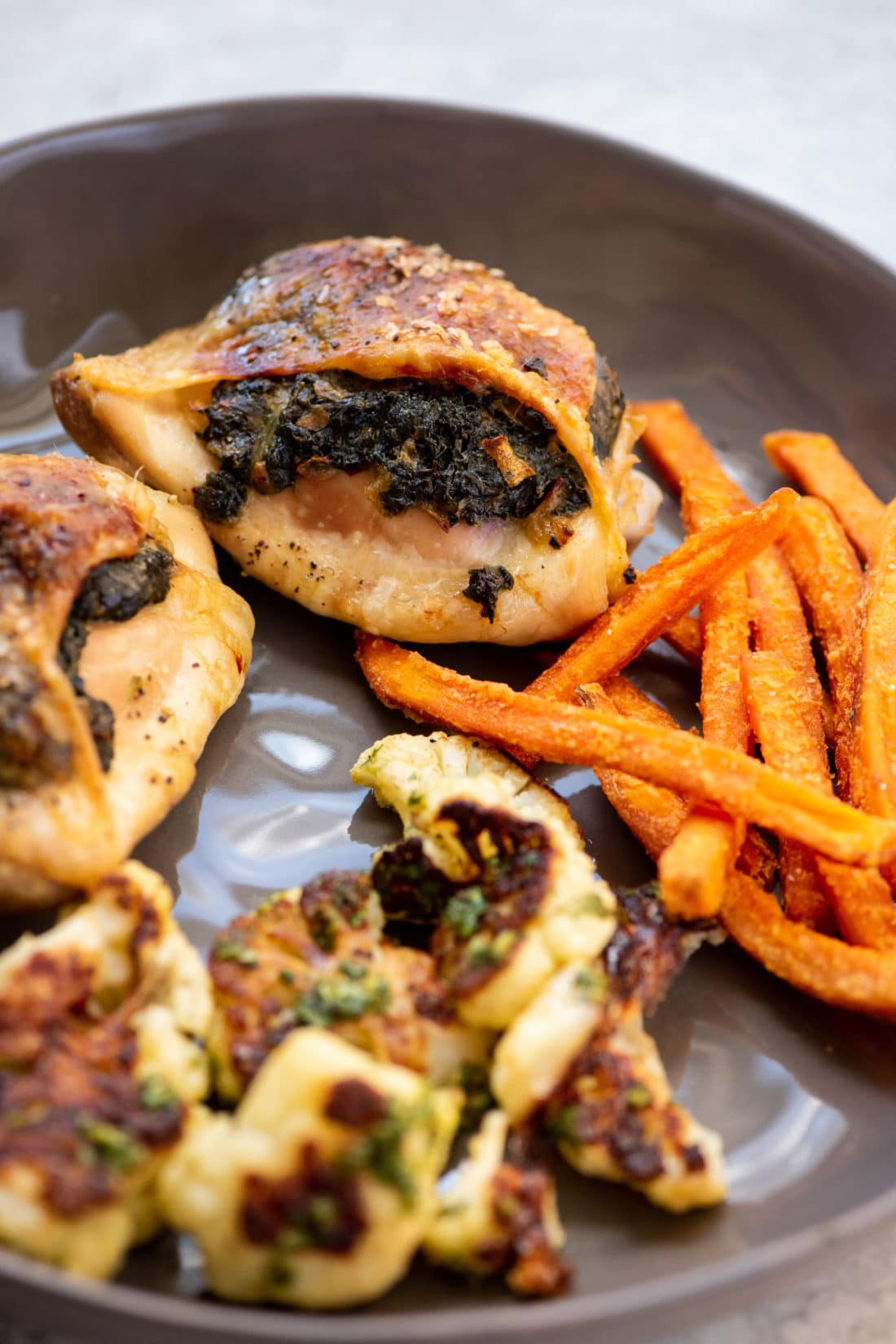 Plate of sweet potato fries, cauliflower, and Creamed Spinach Stuffed Chicken Thighs.