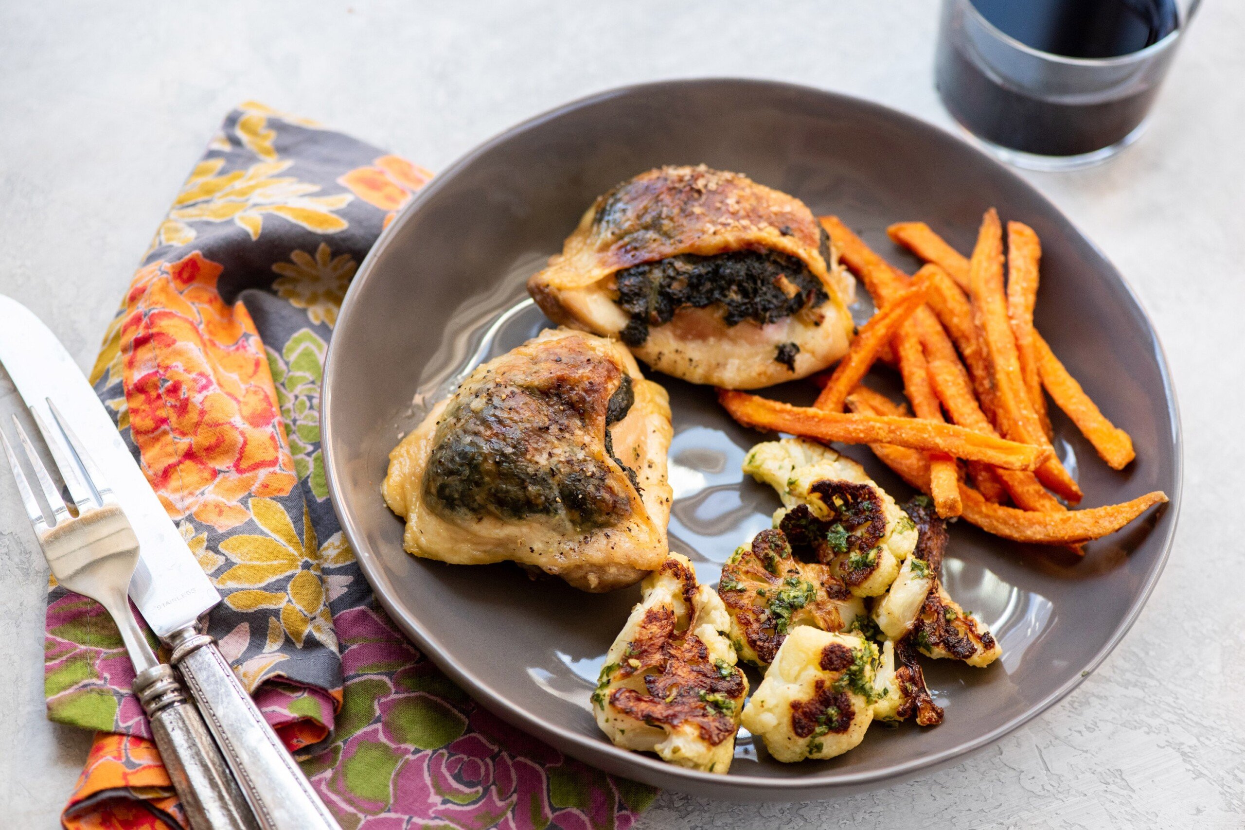 Sweet potato fries, cauliflower, and Creamed Spinach Stuffed Chicken Thighs on a dark plate.