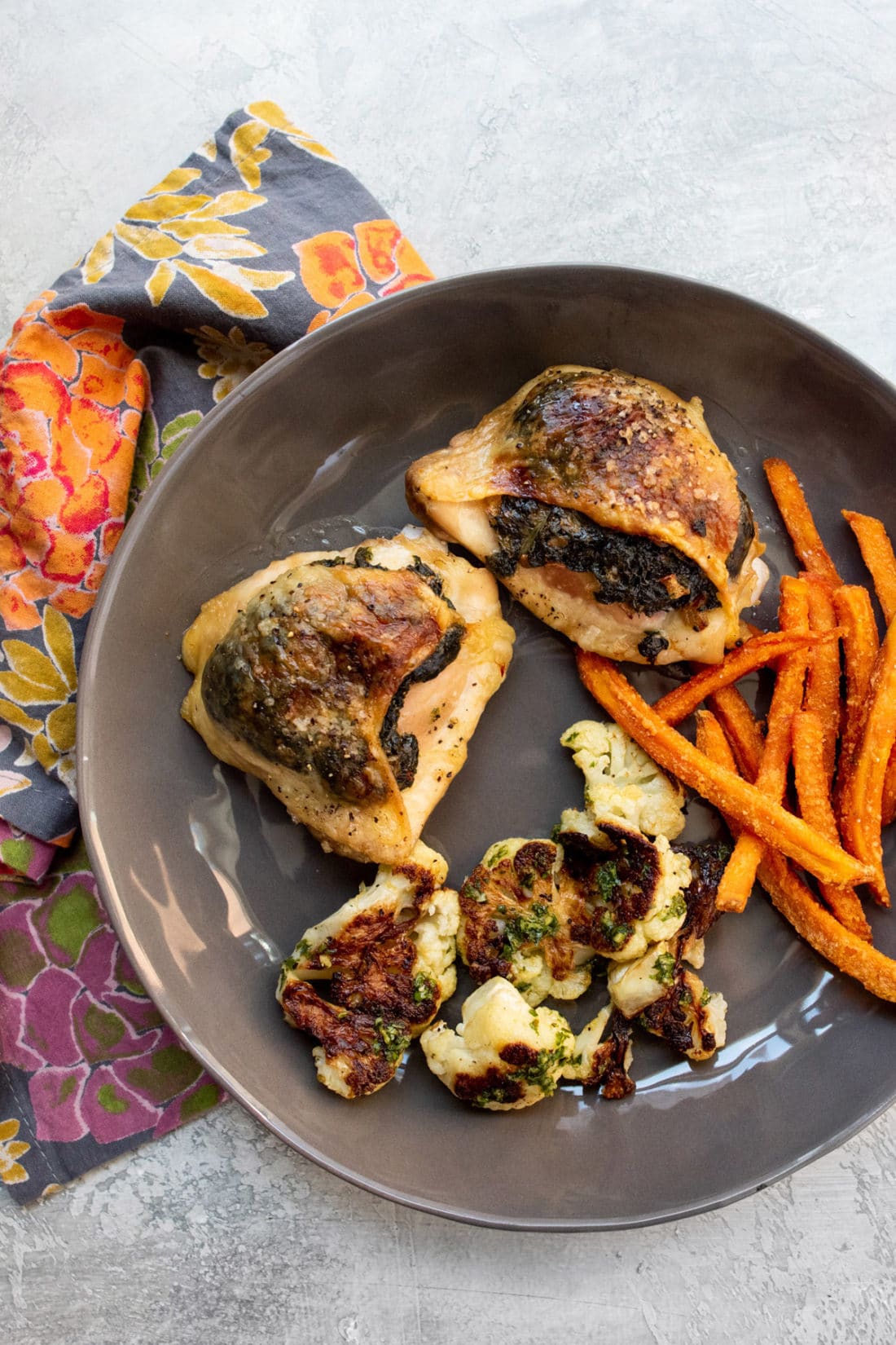 Creamed Spinach Stuffed Chicken Thighs on a plate with sweet potato fries and cauliflower.