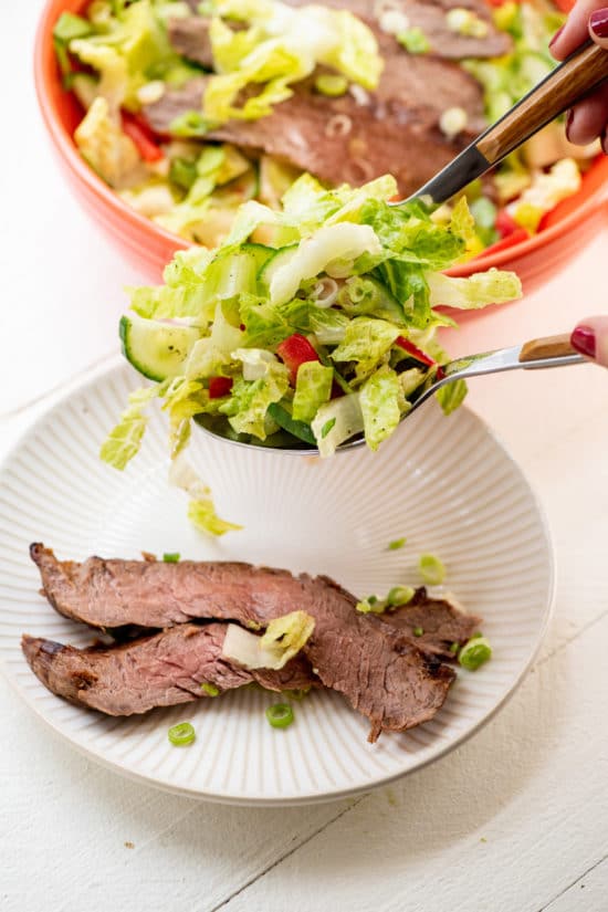 Spoon scooping salad greens onto slices of Smoky Sweet Thai Grilled Flank Steak.
