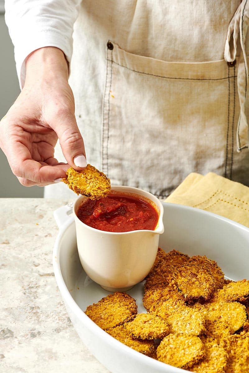 Woman dipping a Baked Zucchini Chip into marinara sauce.