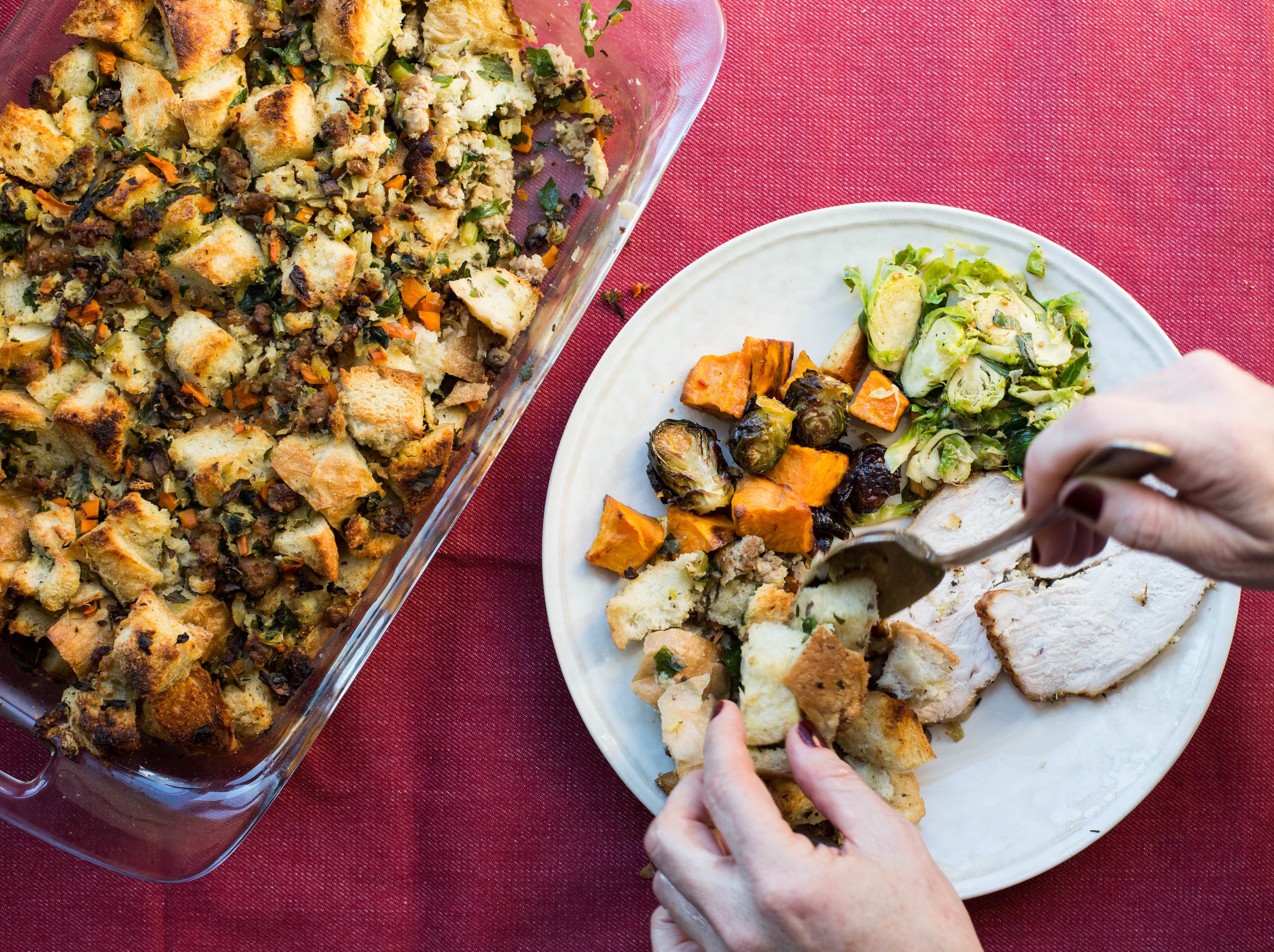 Woman adding Bread Stuffing with Turkey Sausage to a plate with casserole of stuffing nearby.