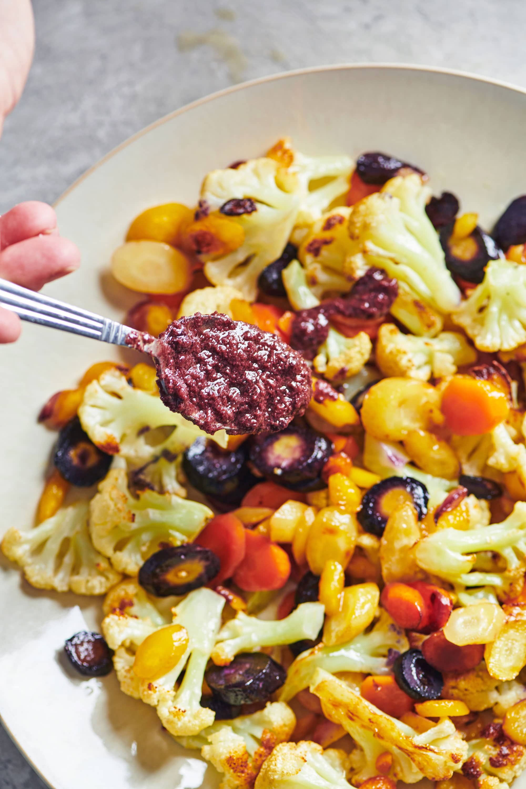 Spooning olive-rosemary dressing over roasted cauliflower and carrots.