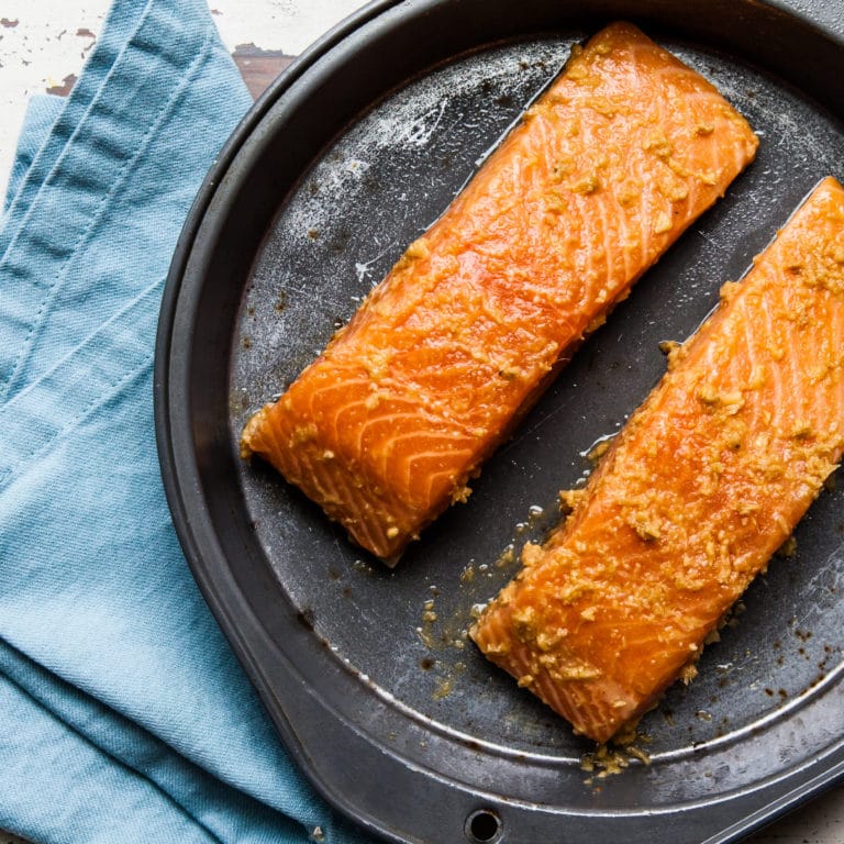 Baked salmon filets with Thai-inspired marinade on baking pan with blue napkin.