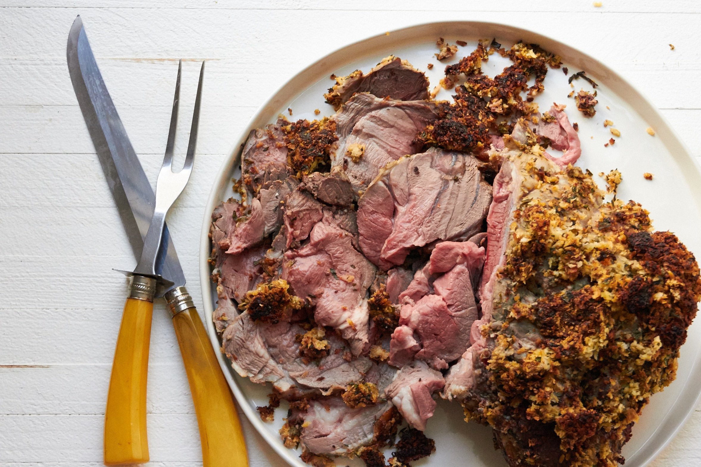 Partially-sliced Herbed Boneless Leg of Lamb with Mustard Crust on a platter.