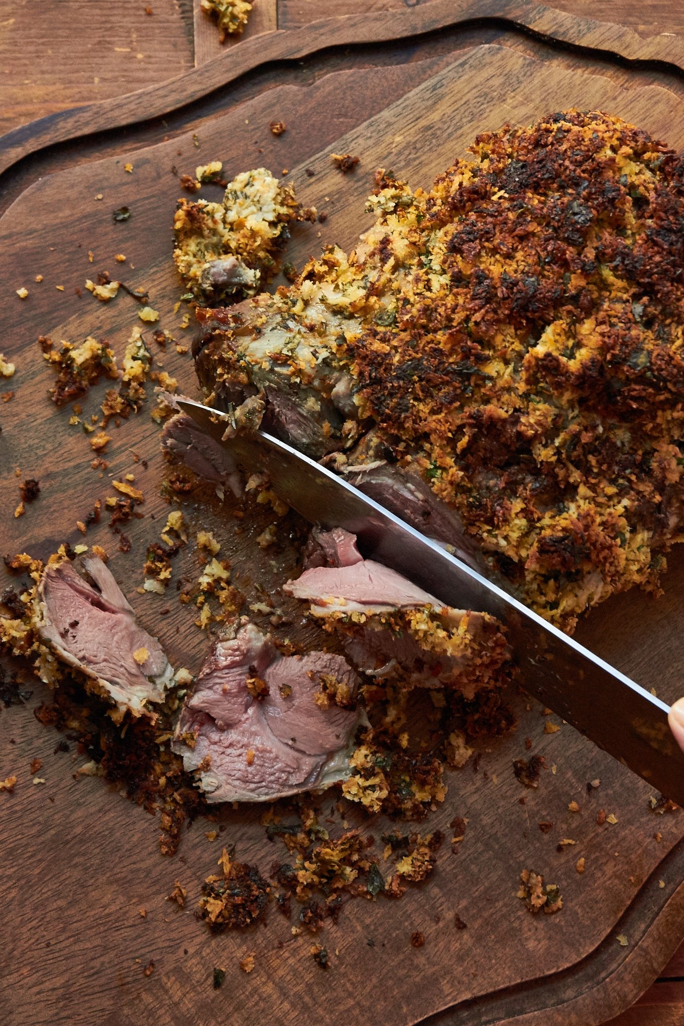 Herbed Boneless Leg of Lamb with Mustard Crust being sliced on a cutting board.