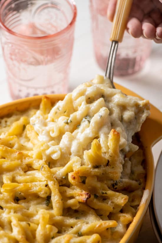 Spoon scooping Creamy Four-Cheese Pasta from a baking dish.