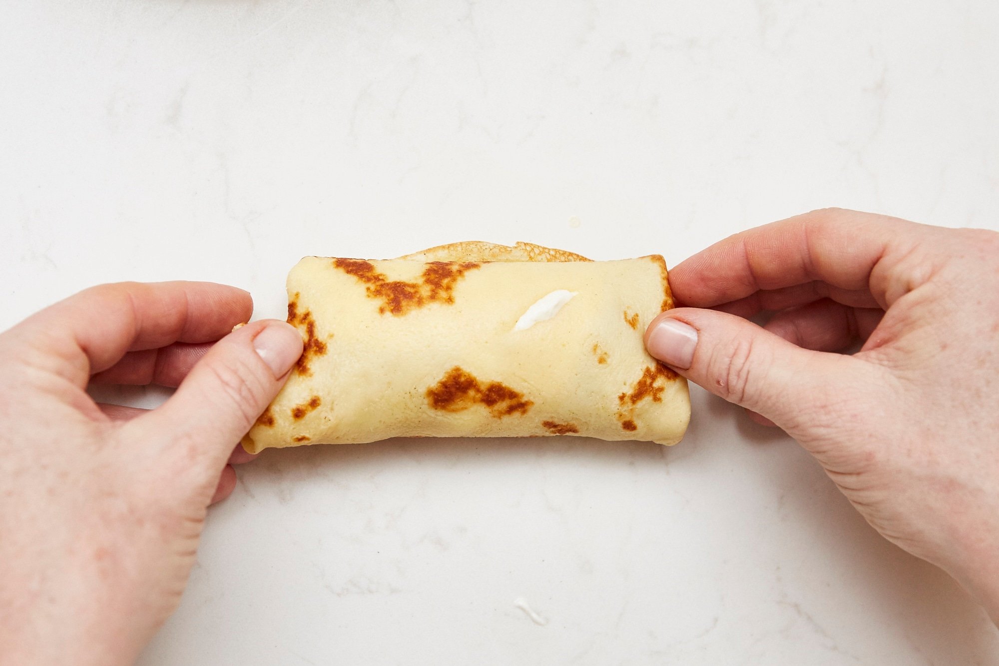 Woman with a crepe rolled around cheese filling.