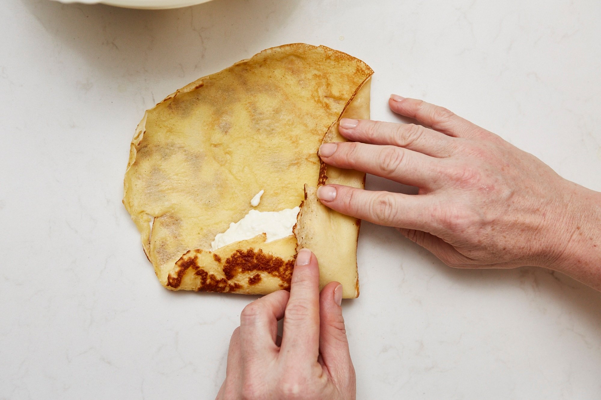 Woman folding the bottom and left sides on a crepe over the cheese filling.