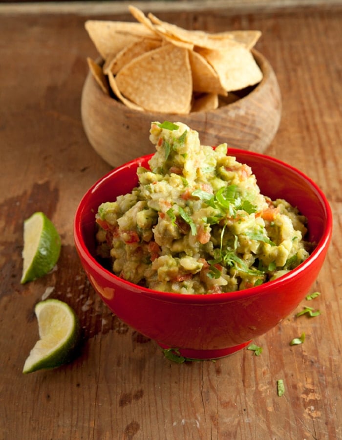 Red bowl of Guacamole next to chips.