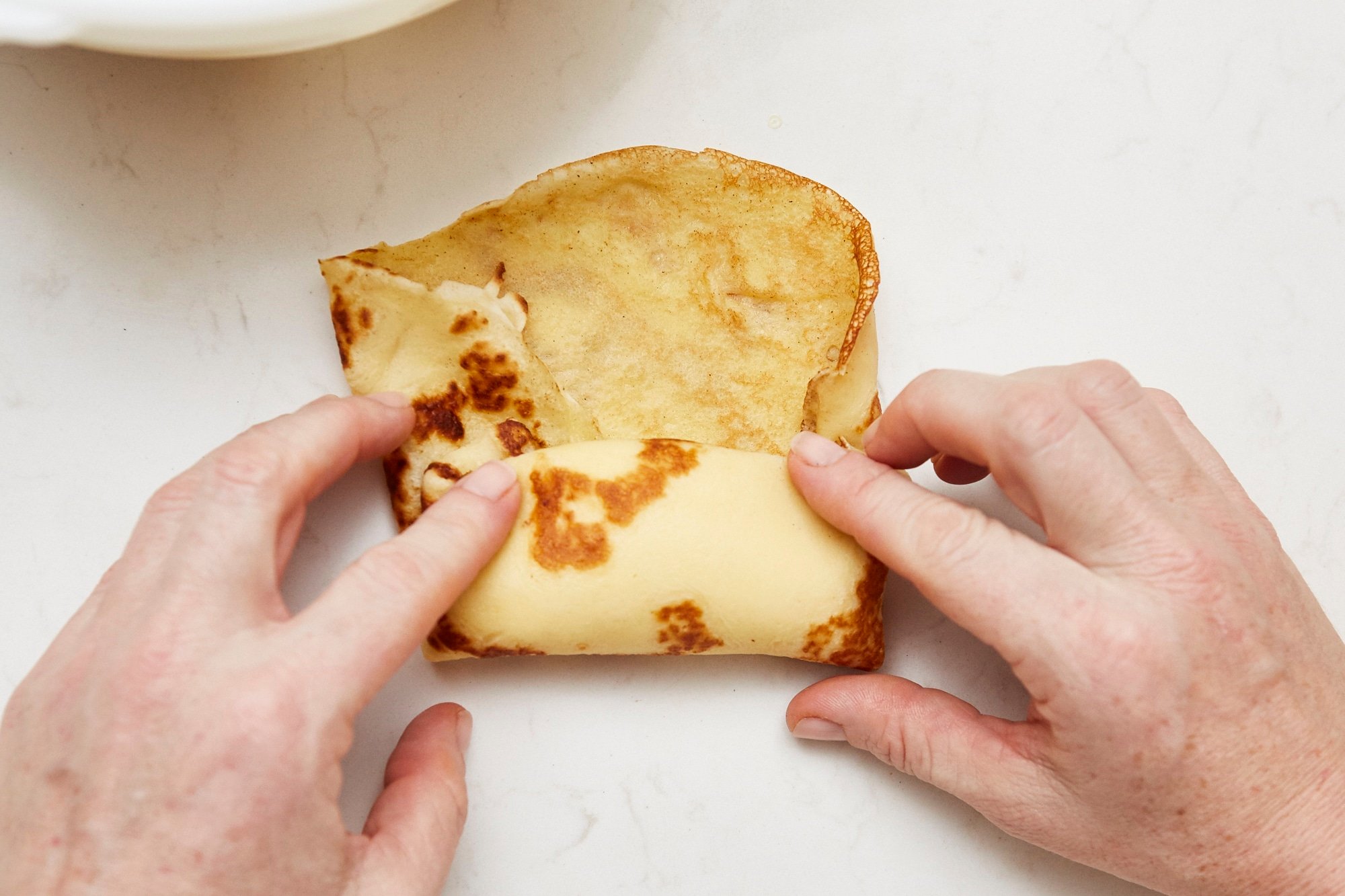 Woman rolling a crepe around the cheese filling.