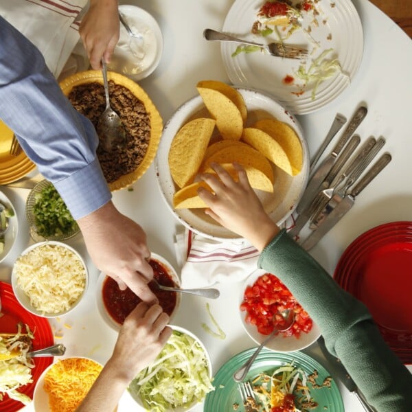 People reaching for various things at a table set with taco fillings.