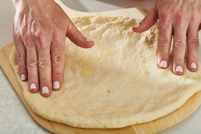 Woman pressing a circle of pizza dough.