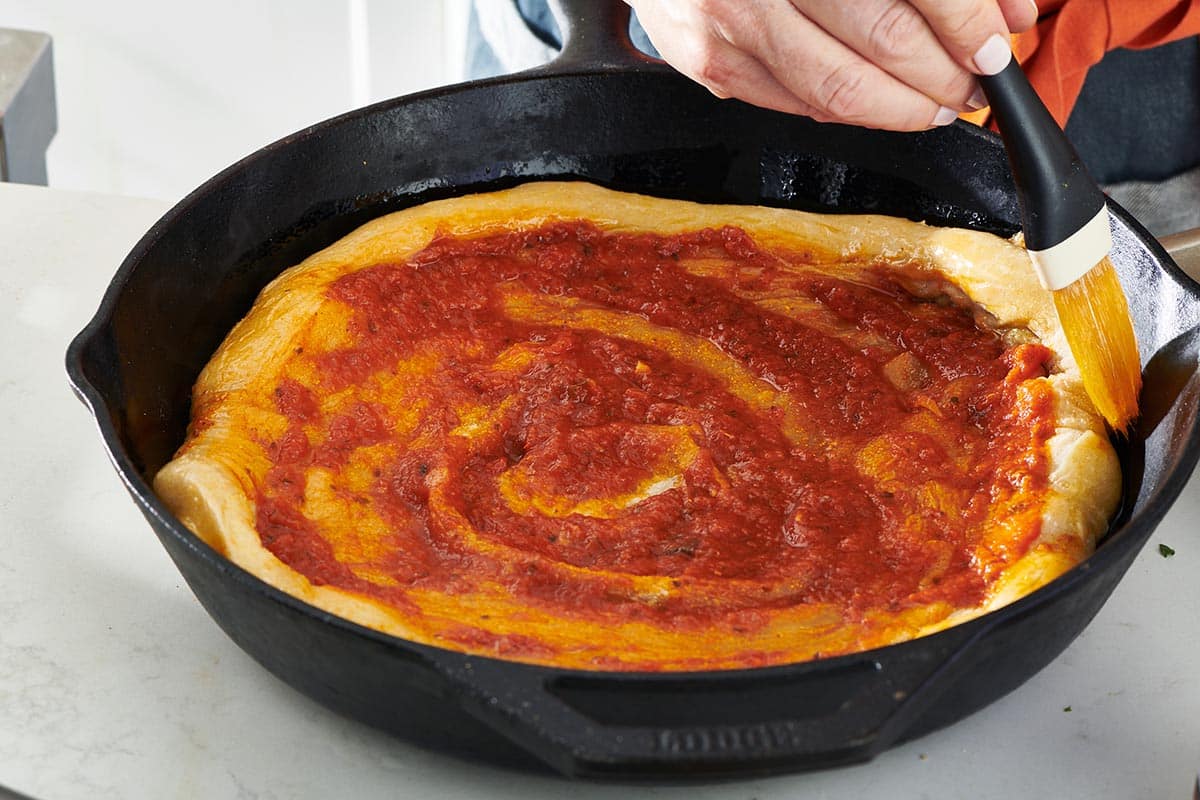 Pizza dough topped with pizza sauce in a cast iron skillet.