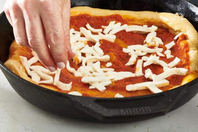 Woman sprinkling mozzarella cheese onto a Cast Iron Pizza.