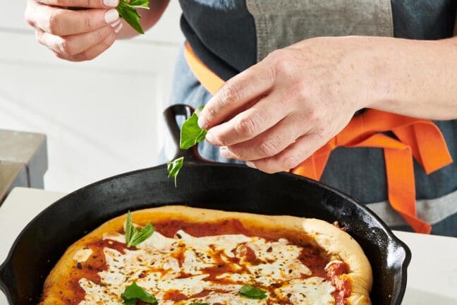 Woman adding basil leaves to a Cast Iron Pizza.