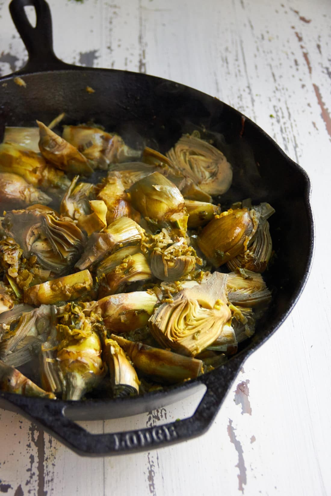 Baby Artichokes braising in a skillet.