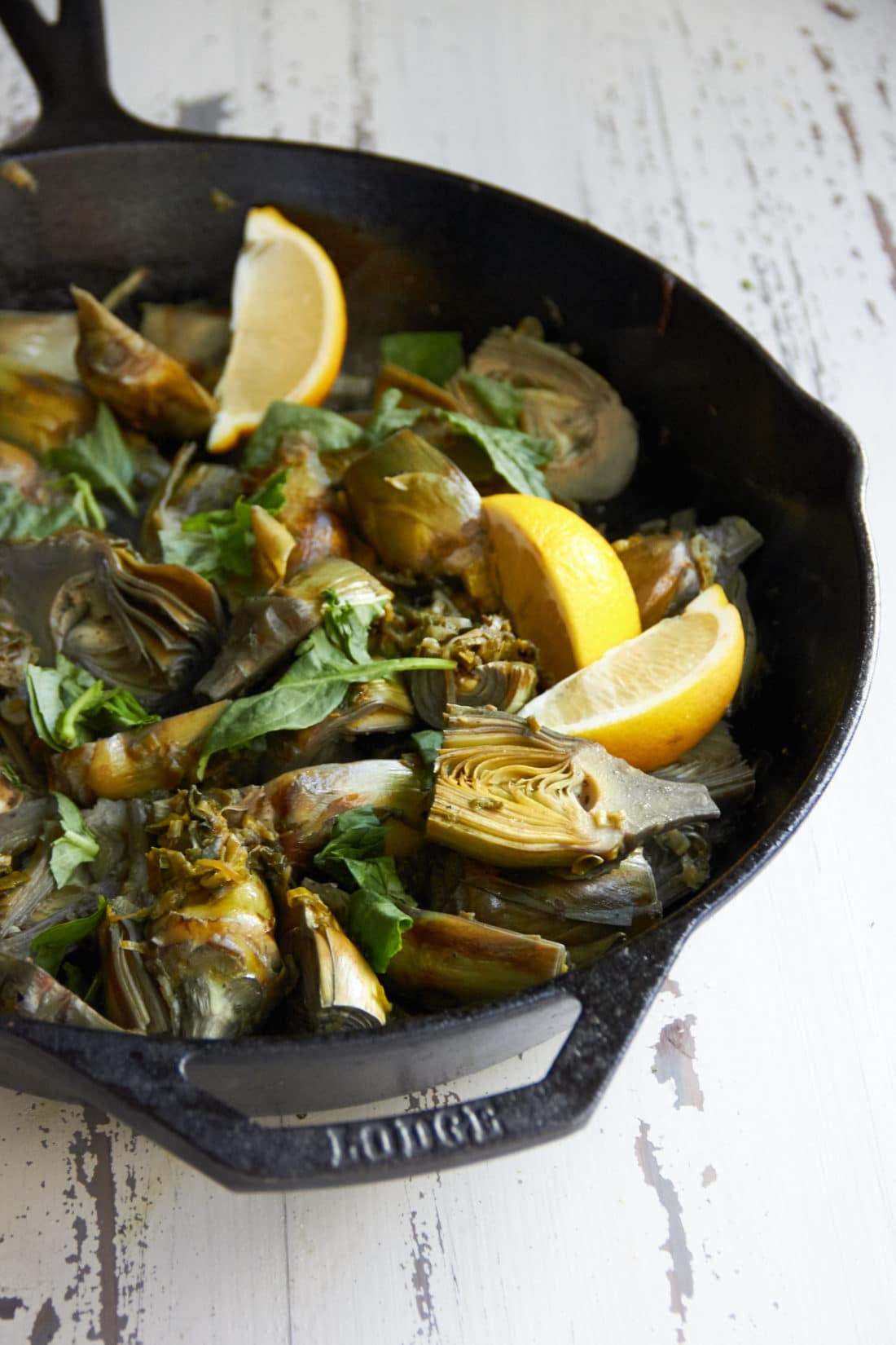 Lemon wedges in a skillet of Braised Baby Artichokes with Leeks and Capers.