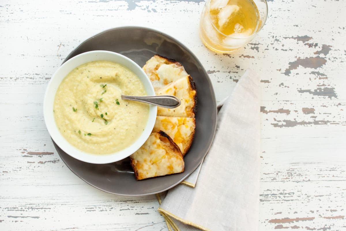 Table with a napkin, glass, and Parsnip and Golden Beet Soup with cheese toasts.