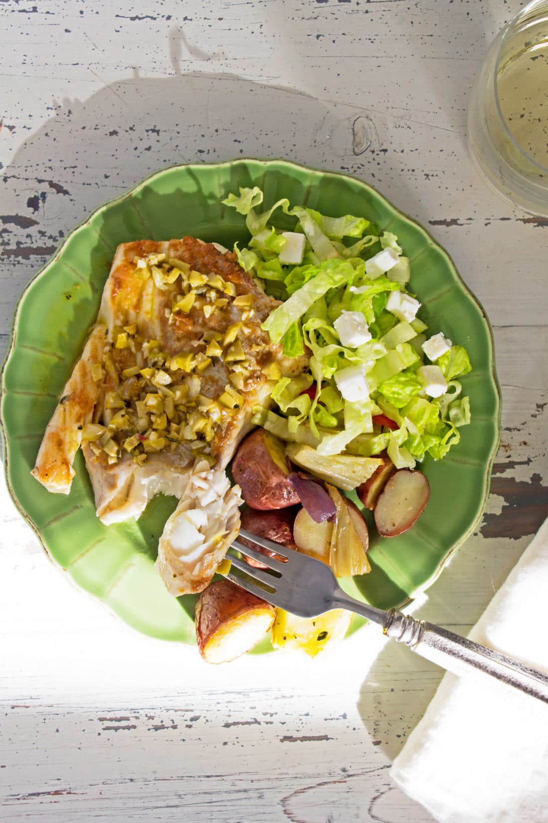 Fork with Rosemary Orange Cod Fillet over a green plate with salad and potatoes.