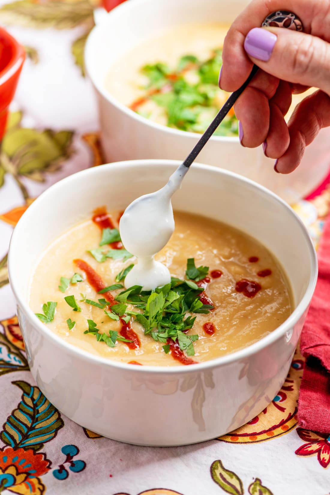 Woman dabbing sour cream onto a bowl of Creamy Rutabaga, Parsnip and Cheddar Soup.