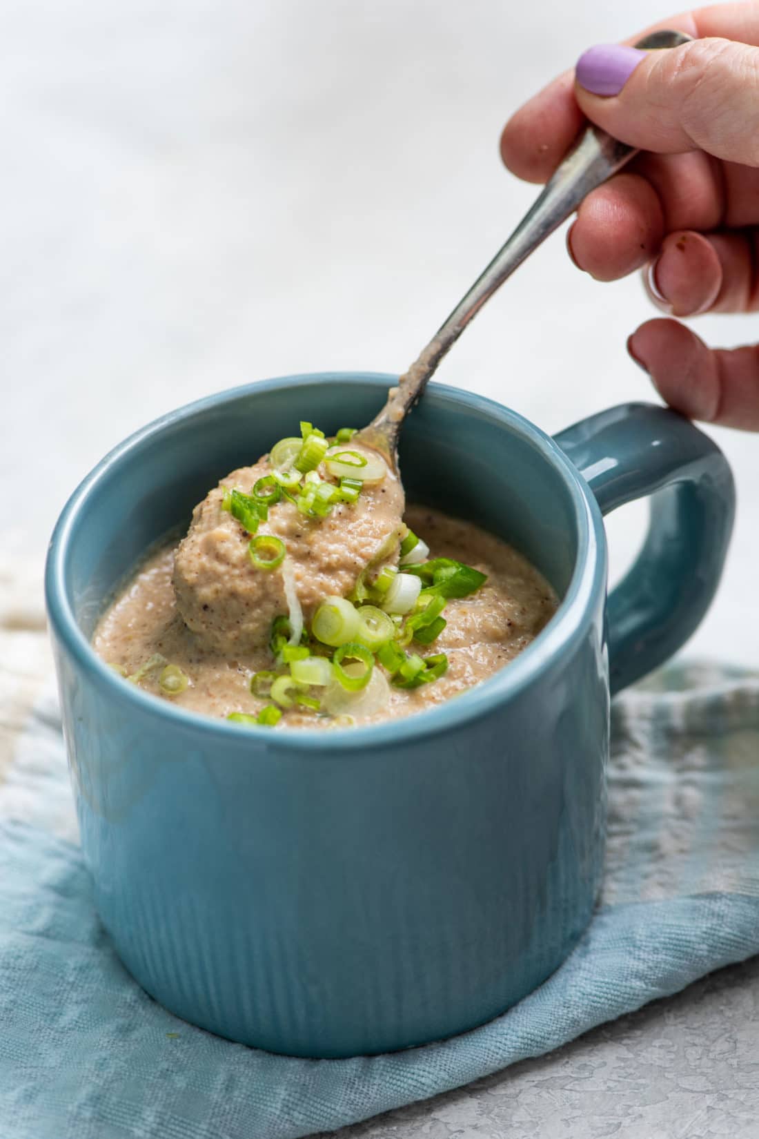 Spoon scooping Roasted Cauliflower and Sunchoke Soup from a mug.