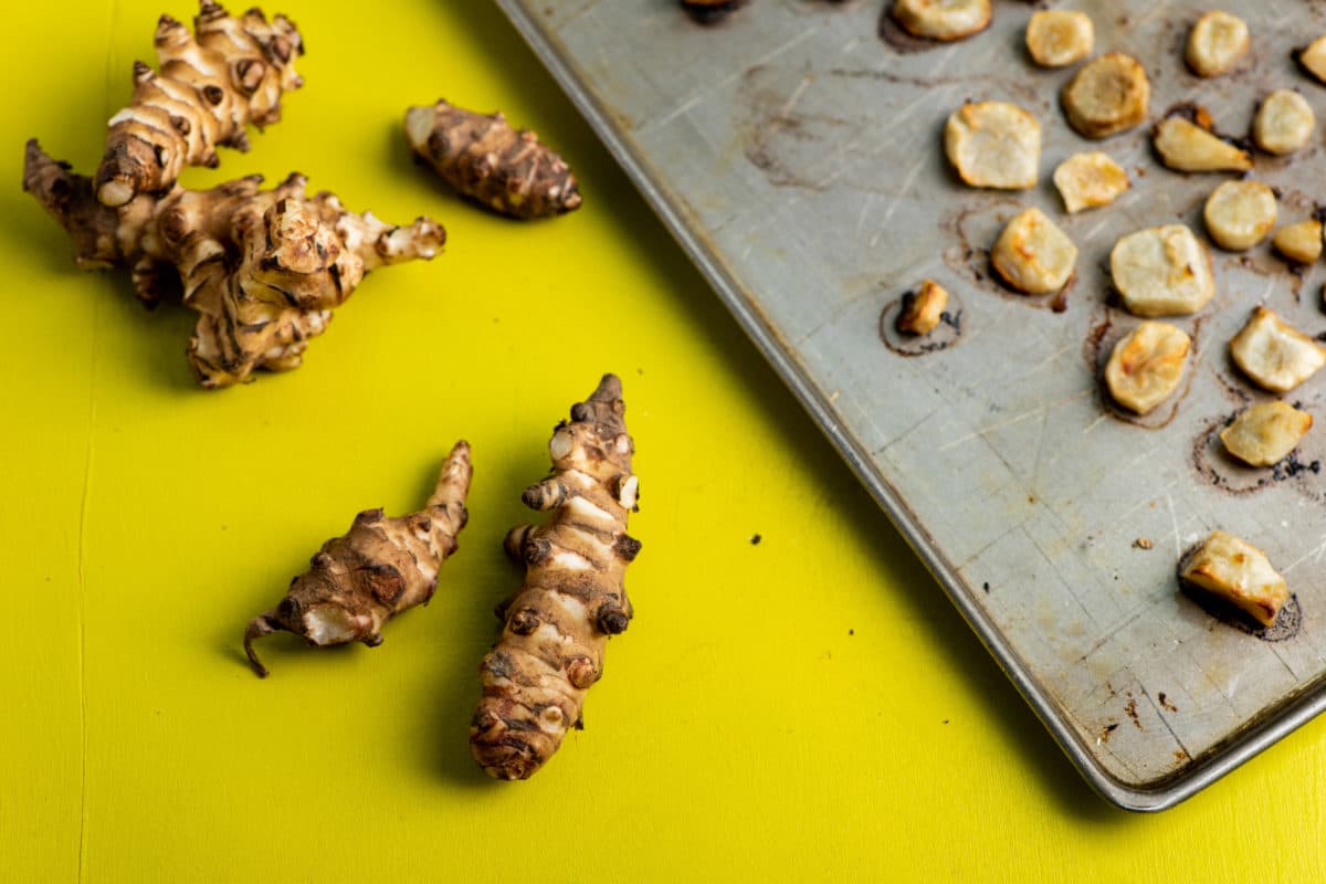 Jerusalem Artichokes on a yellow surface next to a baking sheet.