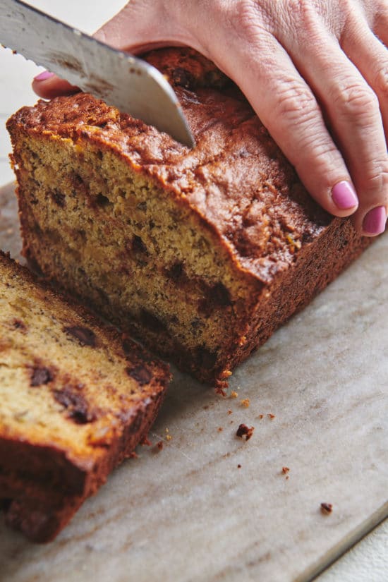 Woman slicing a loaf of Banana Bread with Chocolate and Crystallized Ginger.