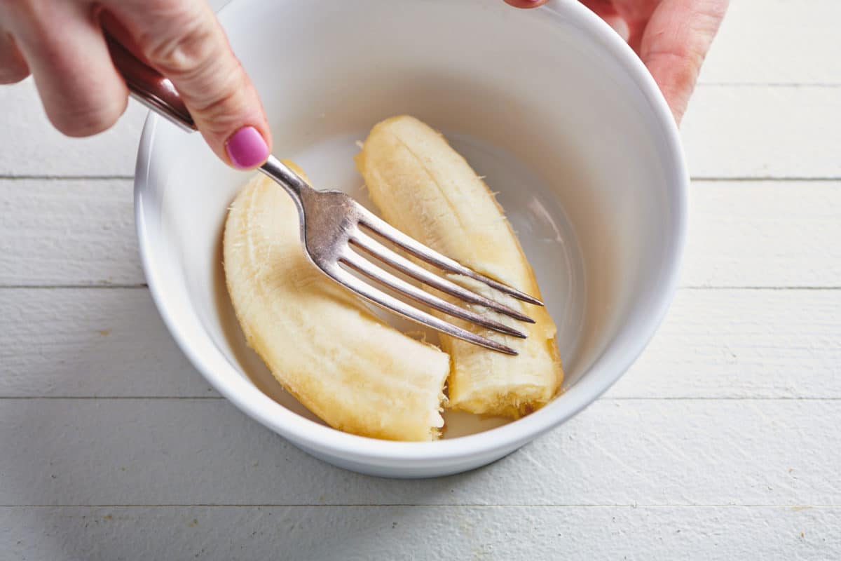 Woman using a fork to mash bananas in a bowl.