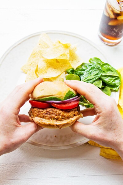 Person holding a Chipotle Barbecue Turkey Burger over a plate with chips and salad.