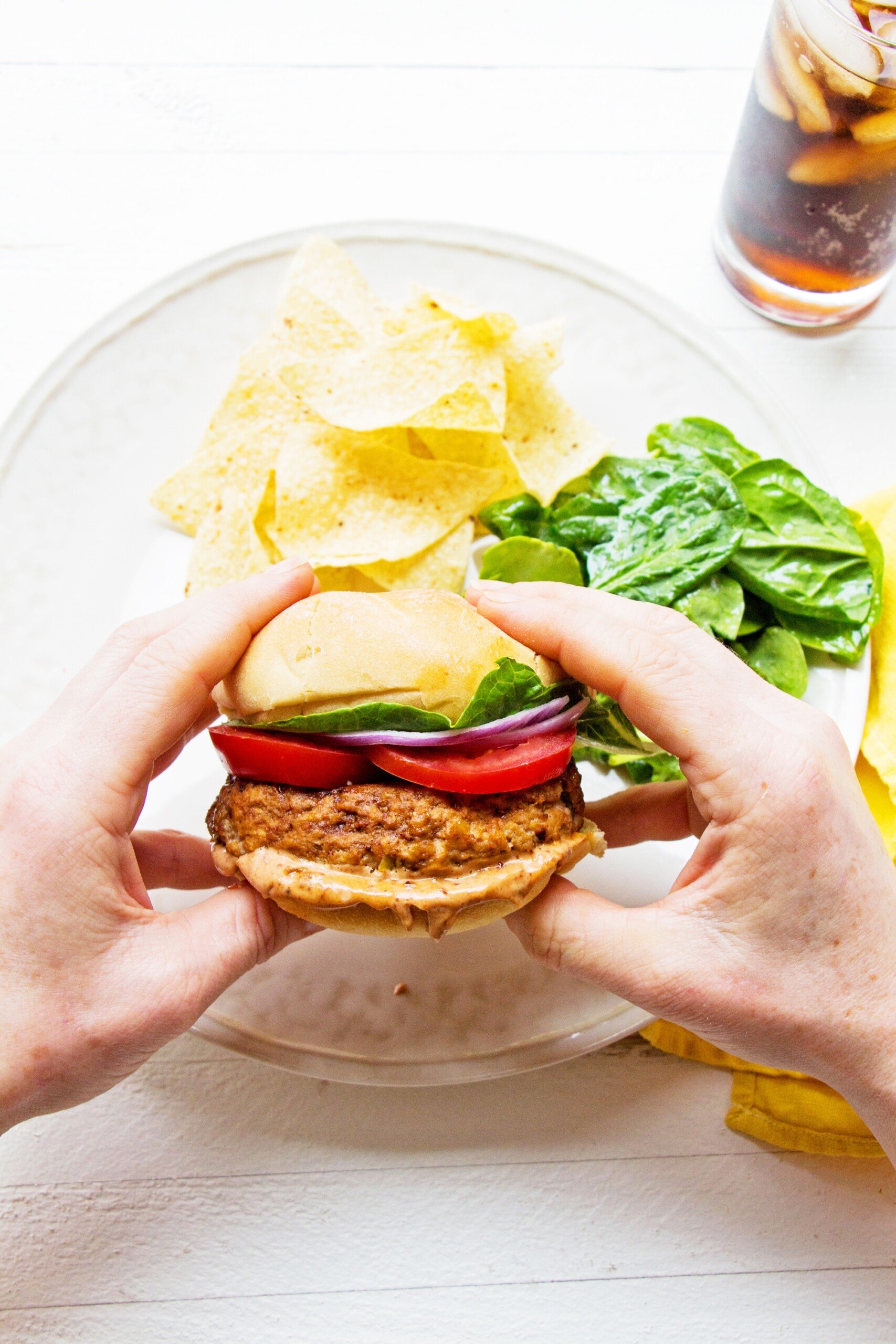 Woman holding a Chipotle Barbecue Turkey Burger over a plate with chips and salad.