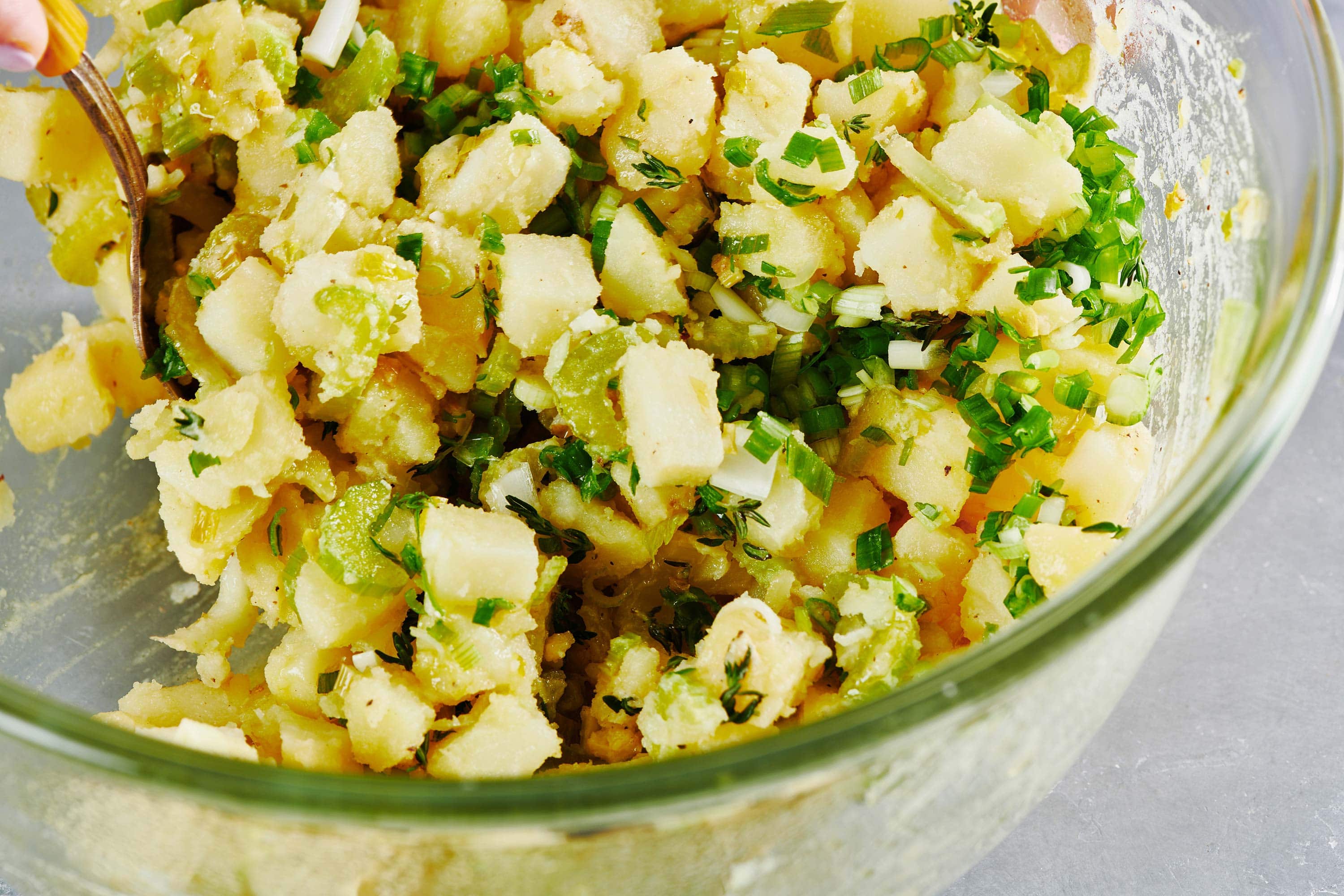 Mixing Vegan Potato Salad with thyme and scallions in glass bowl.