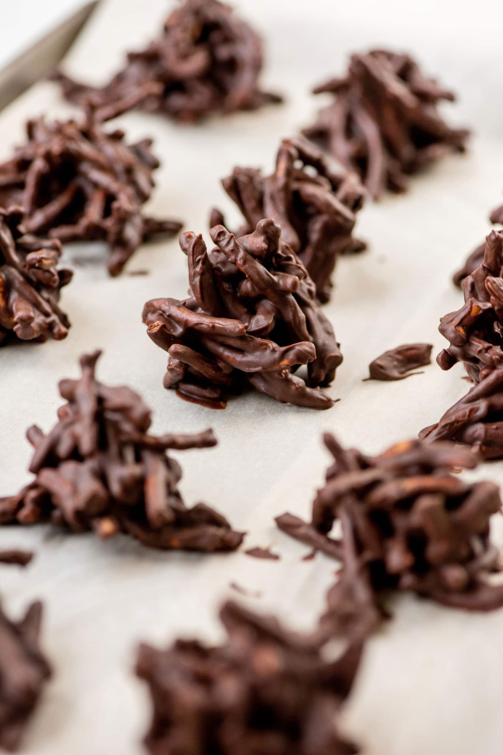 Chocolate, Peanut and Pretzel No-Bake Haystack Cookies on parchment paper.