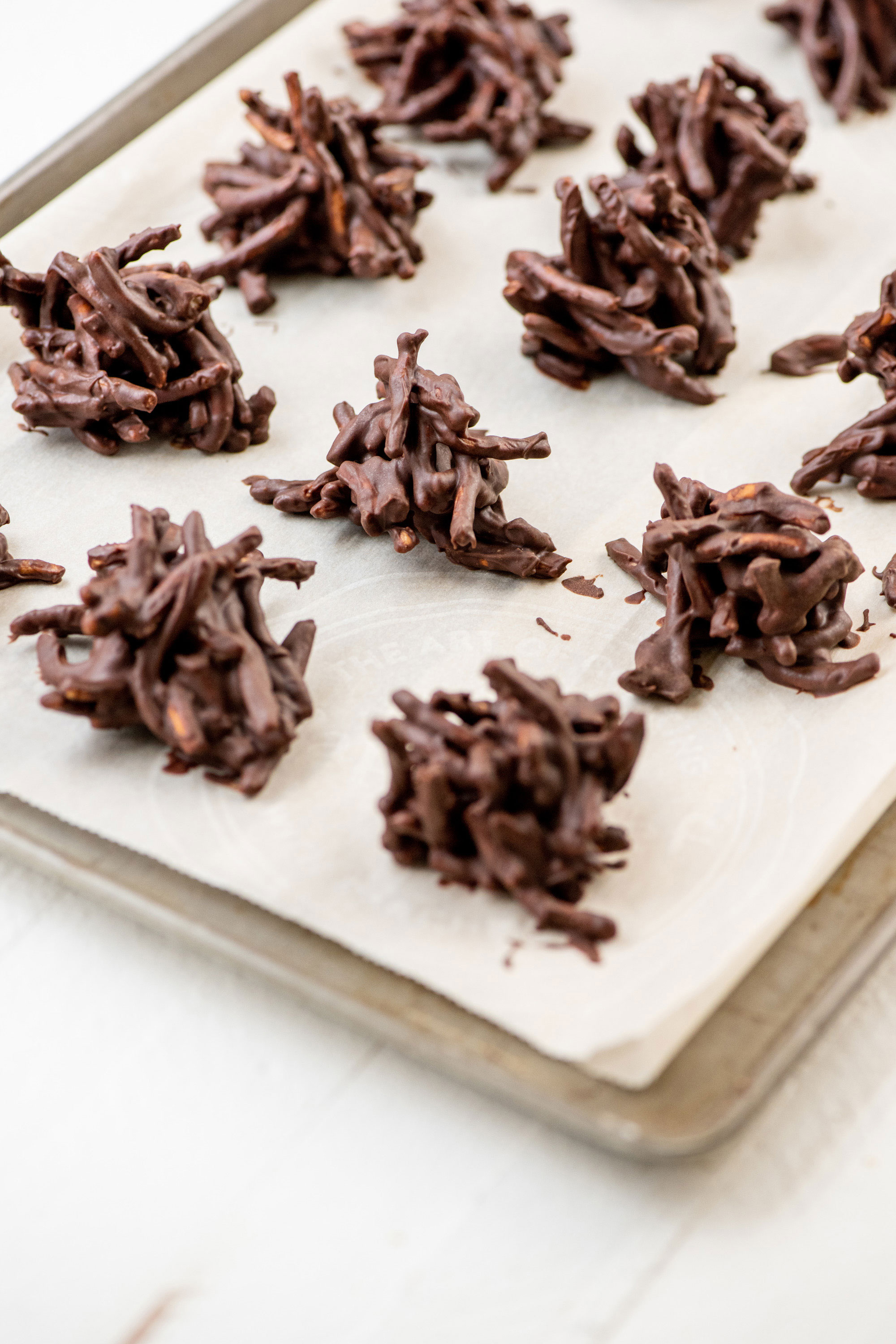 Chocolate, Peanut and Pretzel No-Bake Haystack Cookies on a lined baking sheet.