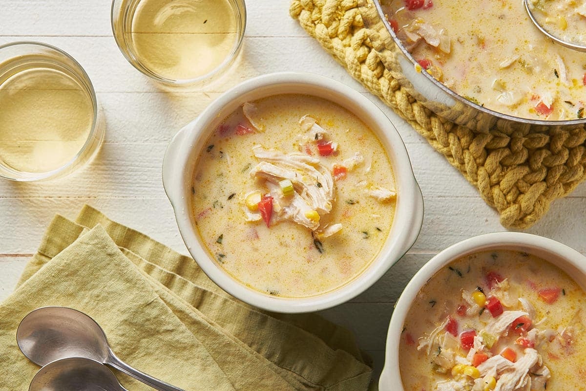 Bowls of Chicken Corn Chowder on a white, wooden surface.