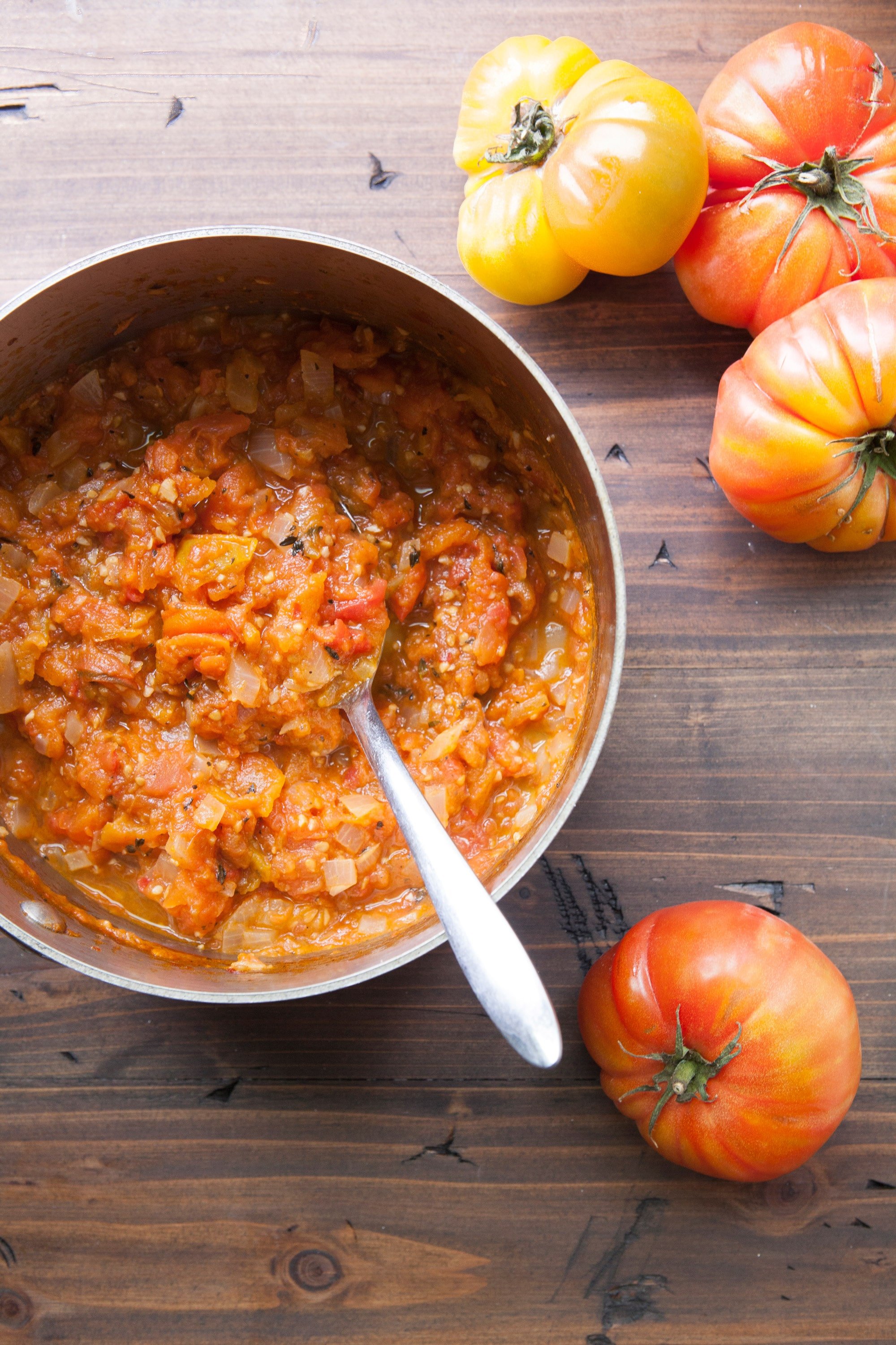 Saucepan with fresh tomato sauce on wood table next to heirloom tomatoes.