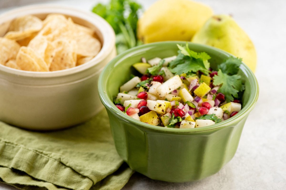 Green bowl of Spicy Pear and Cilantro Salsa and a white bowl of tortilla chips.