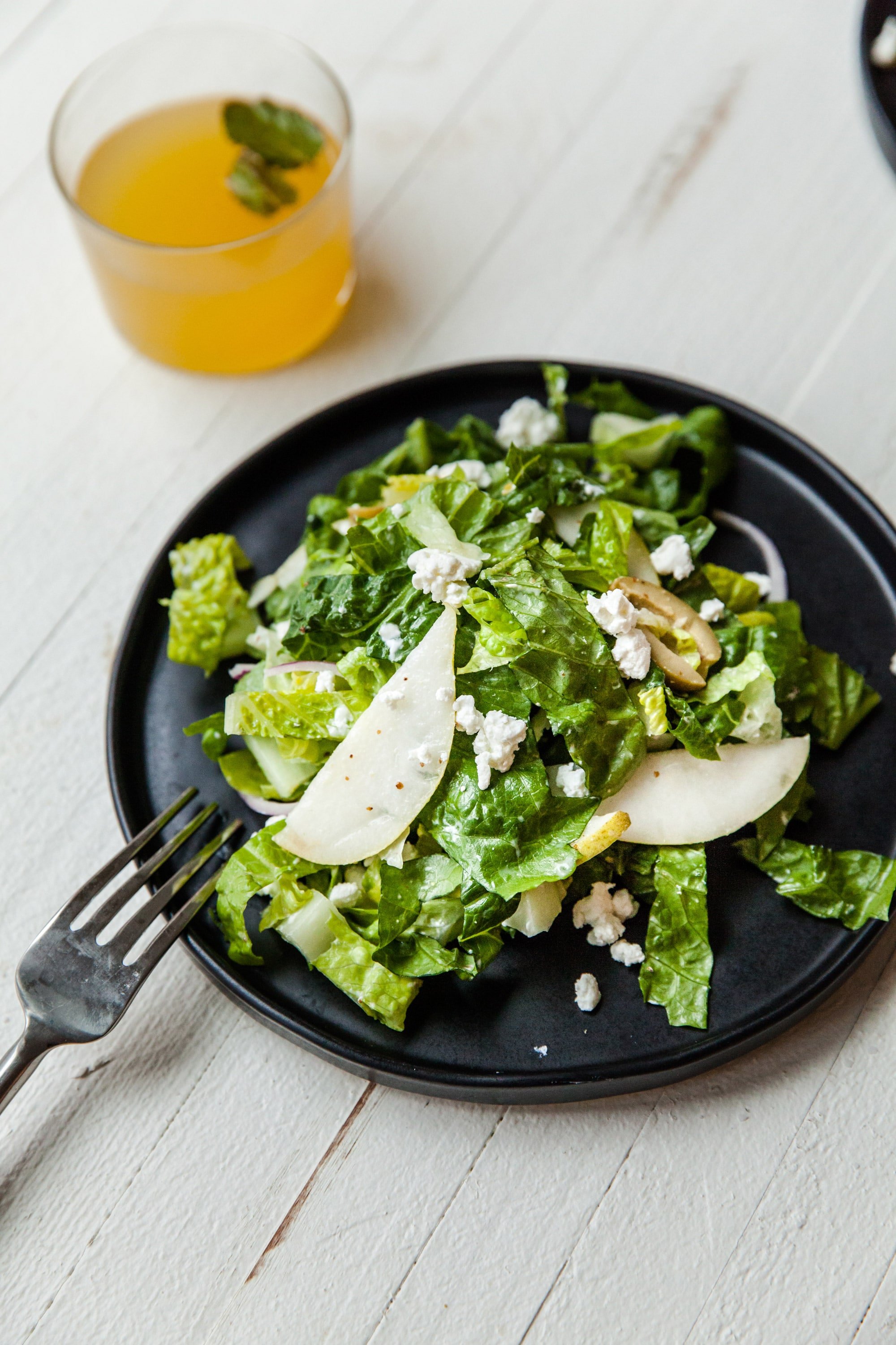 Romaine, Pear and Goat Cheese Salad on black plate with drink.