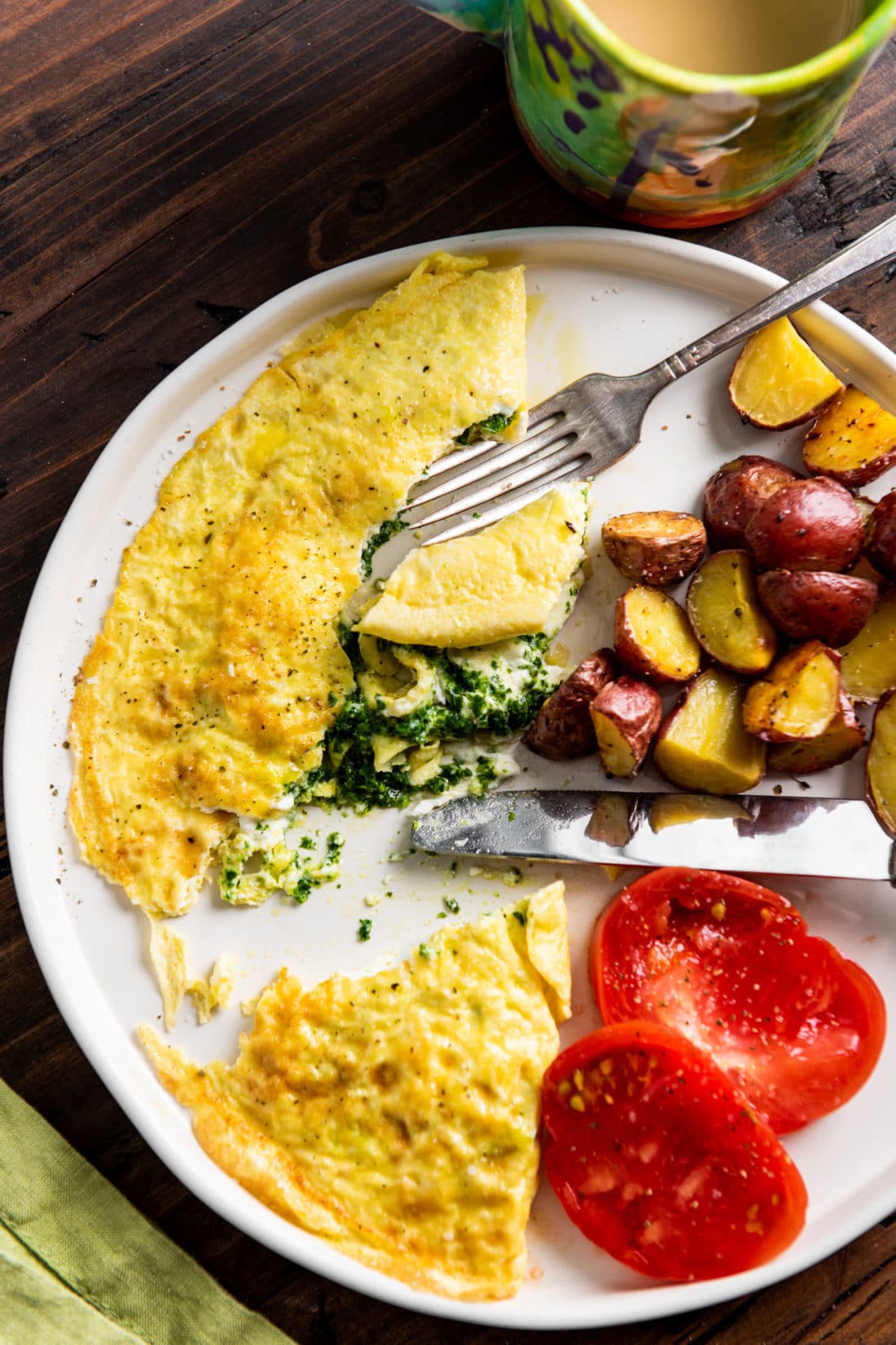 Partially-eaten Kale Pesto and Goat Cheese Omelet on a plate with potatoes and tomatoes. 