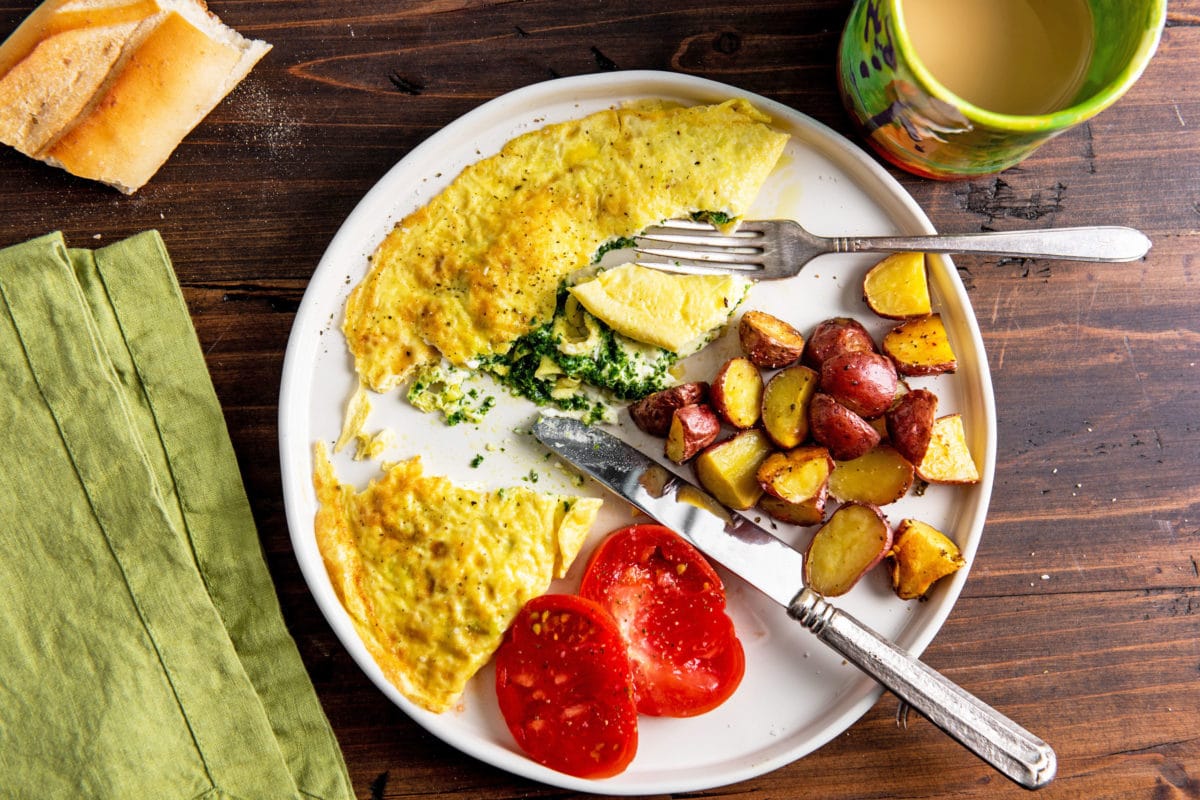 Plate and utensils with a Kale Pesto and Goat Cheese Omelet, potatoes, and tomatoes.