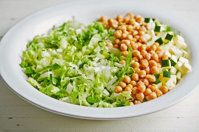 Large plate of chickpeas on lettuce and zucchini.