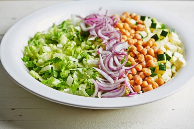 Large plate of red onion and chickpeas over lettuce and zucchini.