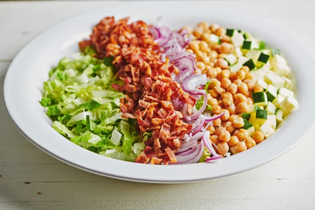 Large plate of bacon, red onion, and chickpeas over lettuce and zucchini.