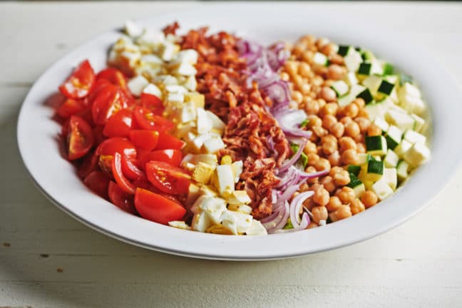 Large plate of tomato, hard-boiled egg, bacon, red onion, and chickpeas over lettuce and zucchini.