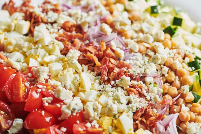 Late Summer Cobb Salad topped with bacon, red onion, crumbled cheese, and other toppings.